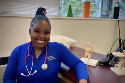 Student Ijjae Hill with stethoscope in PT office with spine models behind her.