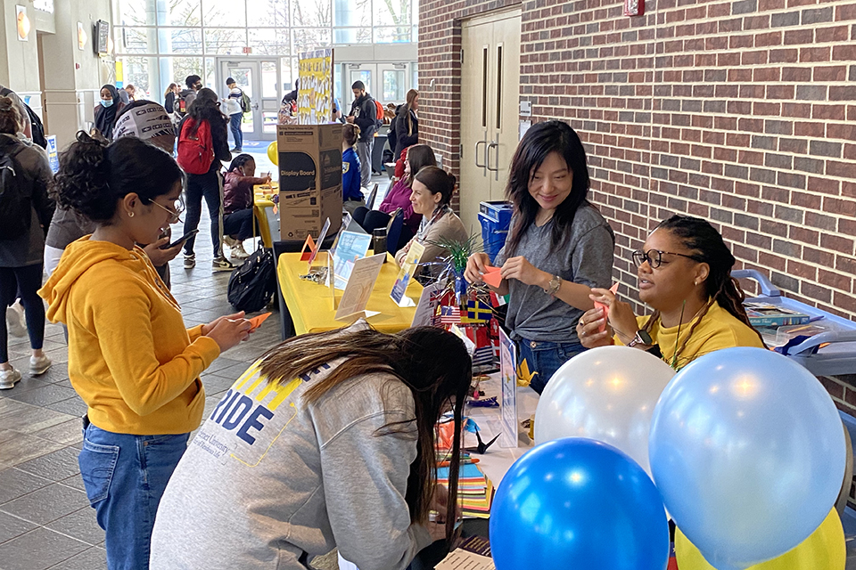 Several students at a Courage Fair table in University Center, with blue and white balloons