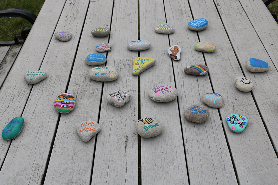 About 20 painted rocks on a picnic table, many with inspirational slogans
