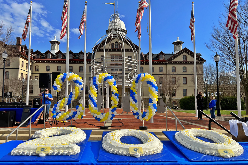 A cake shaped like '200' in front of balloons shaped like '200' with Old Main in the background