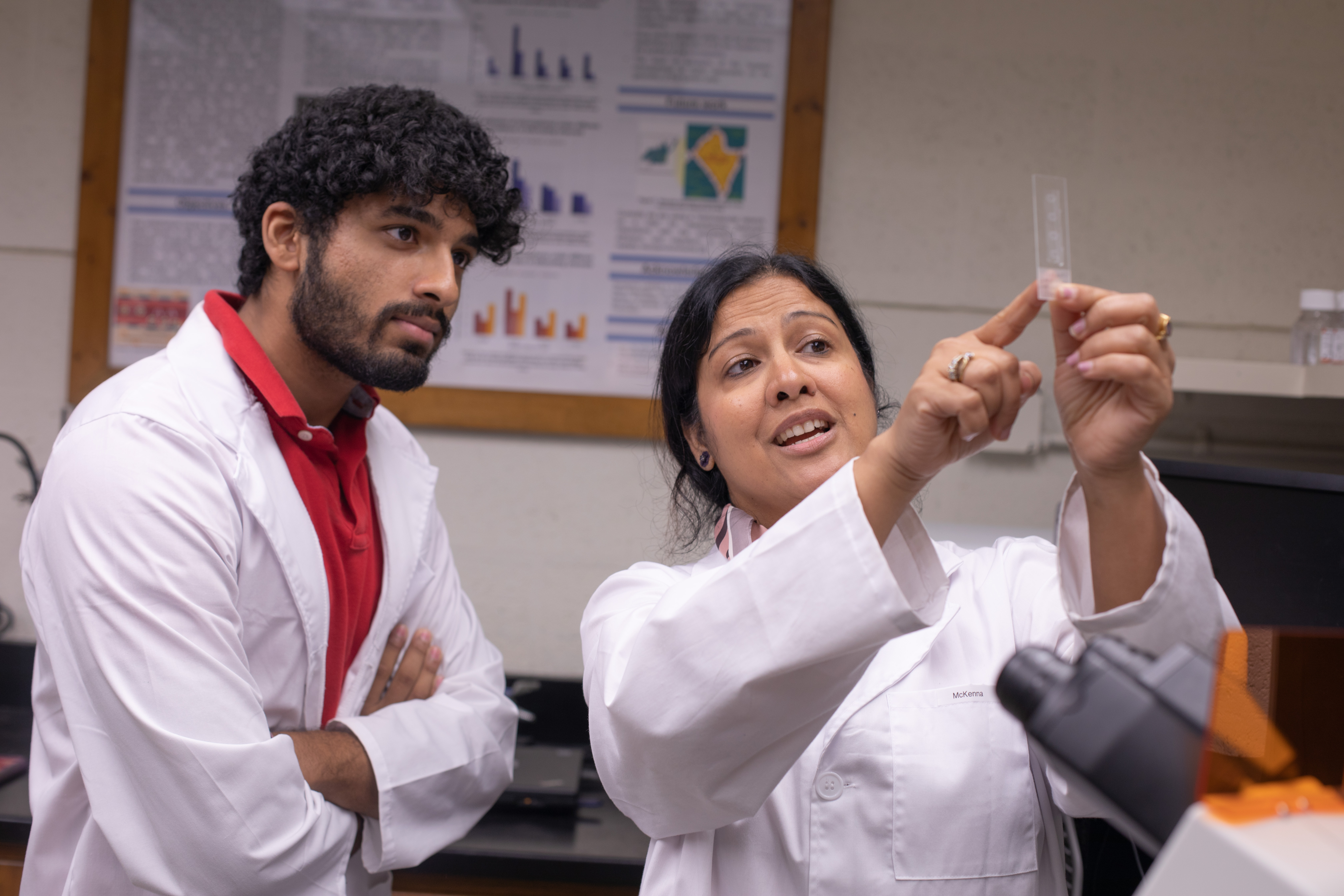 Anita Singh holds up a strip in her lab, while a student observes