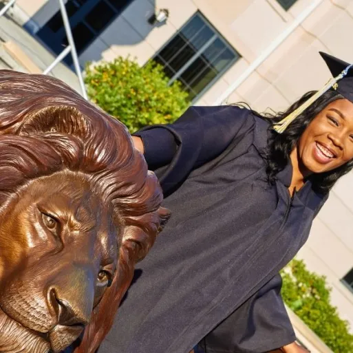 A graduate poses at the Pride statue in her cap and gown.