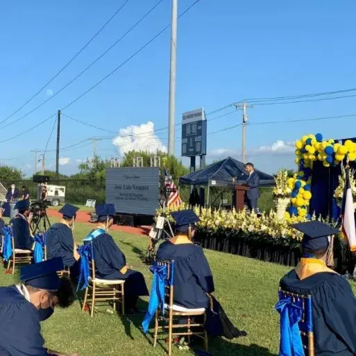 Jose-Luis Vasquez stands on platform in front of high school graduates in caps and gowns