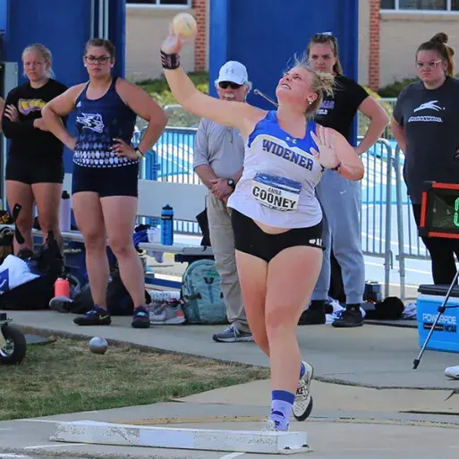Anna Cooney throws a shot put at nationals while wearing a Widener shirt, as other competitors look on