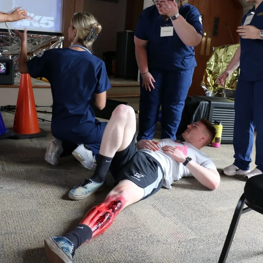 A male student lays on the floor with a simulated leg injury.