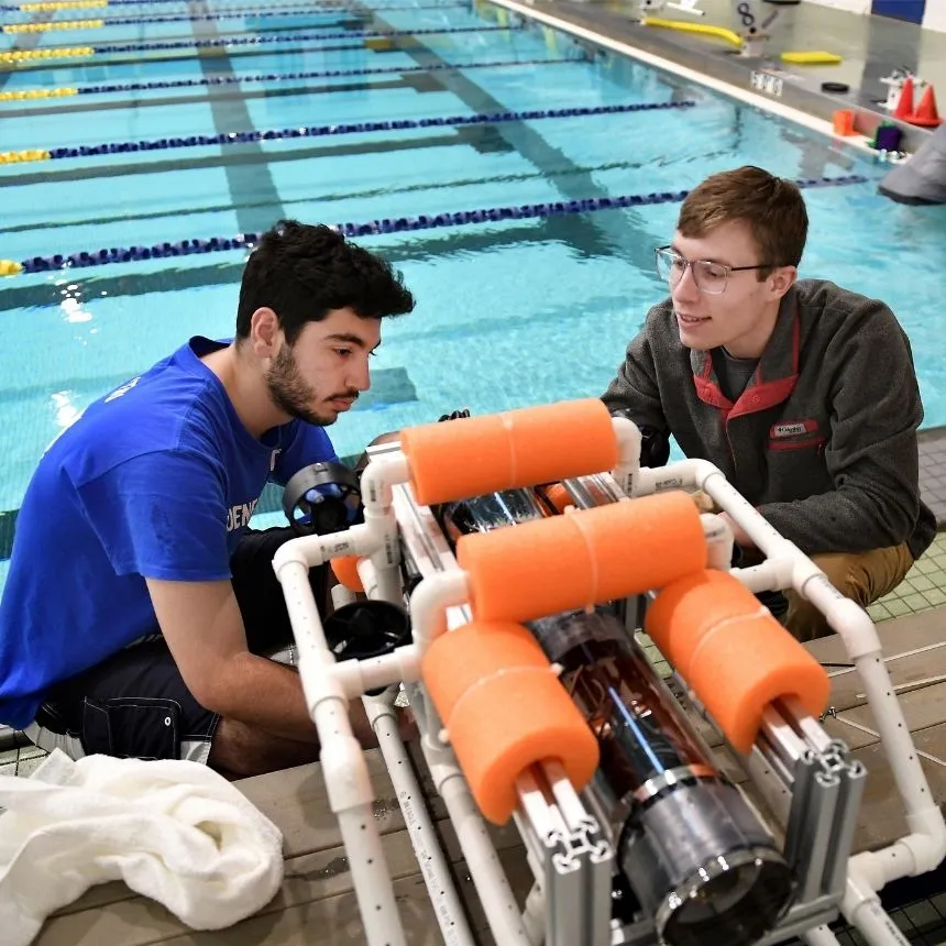 Two male students manually work on a submarine before putting it in the pool to test.