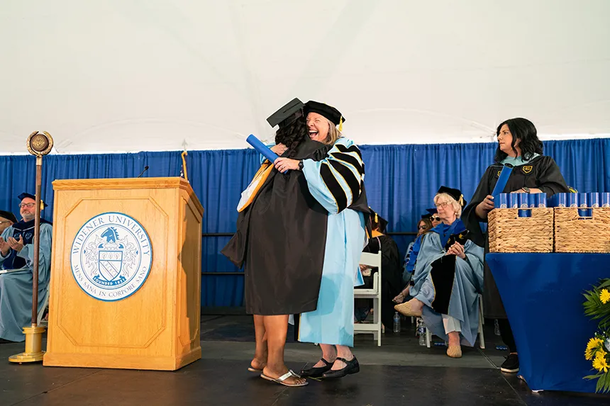 A grad in black cap and gown hugs President Robertson on stage