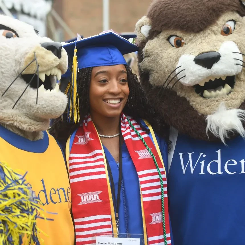 A female graduate poses in between the mascots, Chester and Melrose.