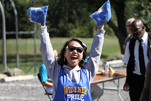 Student in sunglasses at Widener homecoming with arms in the air celebrating