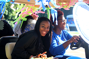 Two Widener students in a colorfully decorated golf cart driving on the track as part of the student organizations golf cart parade.