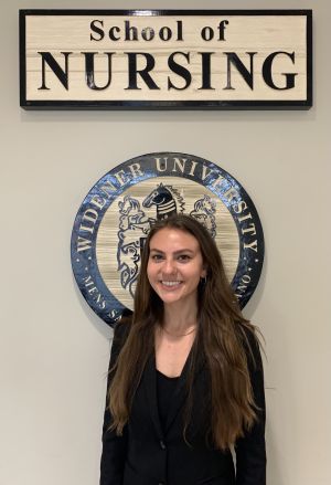 Head shot of student Natalie Sassi with School of Nursing sign and seal behind her.