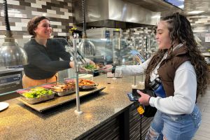 Dietitian Nora Abraham in the kitchen handing a plate of food to student Maritza Garcia ’25