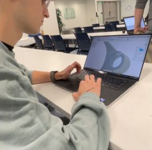A student works on the 3D printing software to design the phone reacher.