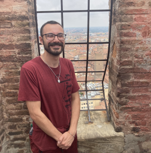 Gianni stand next to an iron bar window overlooking a town