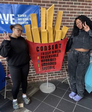 Two Widener University students pose beside a giant red carton of French fries displaying the FRIES acronym for consent: Freely Given, Reversible, Informed, Embodied, and Specific.