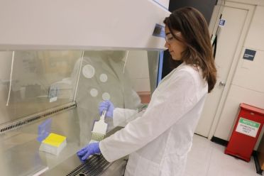 Female student in a lab coat with goggles on conducting research