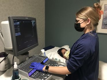 Danielle Laskowski works at a sonography computer screen with a patient in the bed next to her