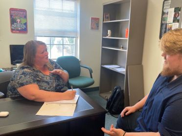 An online MSW student is seen sitting at a desk working with a client.