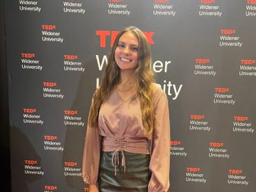 Natalie Sassi poses in front the TEDxWidenerUniversity banner after giving a talk on stage.