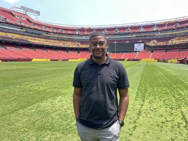 Alumnus Andrew Proctor stands on the field at the Washington Commanders football stadium