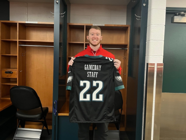 Tiernan poses holding a Philadelphia Eagles jersey that reads "gameday staff"