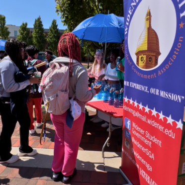 Members of S-G-A stand at a table next to an organization banner and speak to students at the Involvement Fair