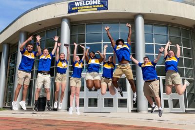 Student orientation leaders in matching blue and yellow shirts jumping in mid-air in front of University Center