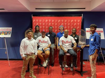 Business students pose with several members of the Phillies organization and the World Series trophies