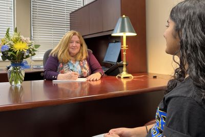 Dean Sarah Swager sits at a desk and speaks with a student sitting across from her.