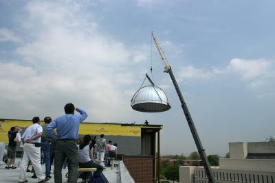 A crane lifts the observatory dome into the roof while spectators watch
