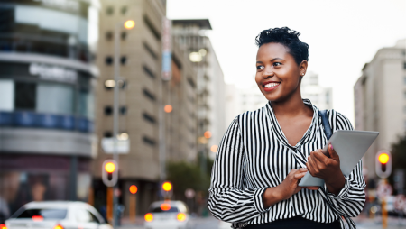 adult student walking in busy city with ipad