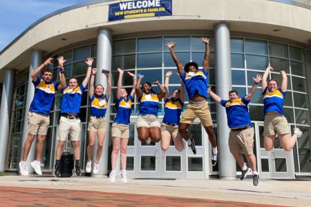 Student orientation leaders in matching blue and yellow shirts jumping in mid-air in front of University Center