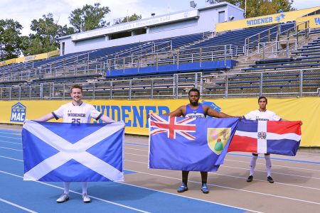 Three international student athletes stand on the stadium track holding their country flags