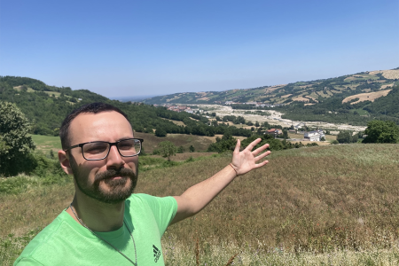 A selfie of Gianni posing with his arm out over a field of grass