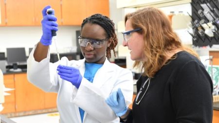 Student in white lab contact conducting experiment while professor oversees