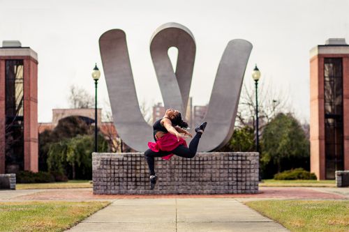 Dance student in a mid-air jump in front of the 'W' statue