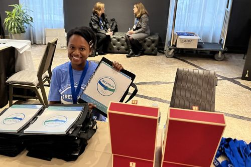 A student holds up materials while sitting at a registration table at a conference