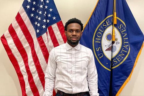 Student Kelvin Smith stands in front of an American flag and a House of Representatives flag
