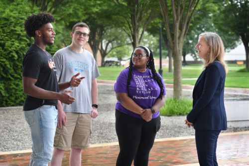 President Stacey Robertson talking outdoors with three students.