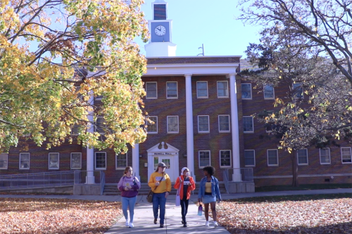 Four students walking away from Howell Hall on a fall day