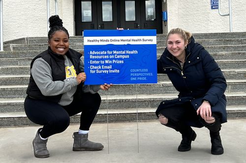 Mental Health Survey Sign 960x640 Two students pose with a law sign about a mental health survey