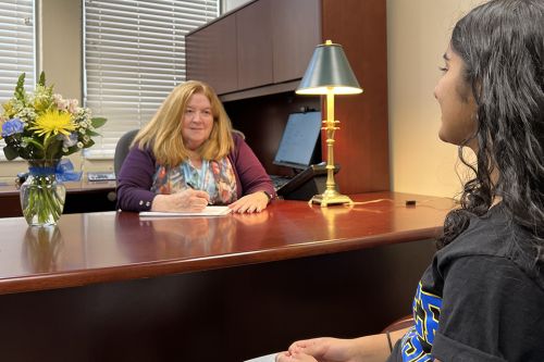 Dean Sarah Swager sits at a desk and speaks with a student sitting across from her.