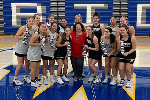Professor Donna McCloskey with members of the women's basketball team at Schwartz Athletic Center; each player is holding a pair of socks