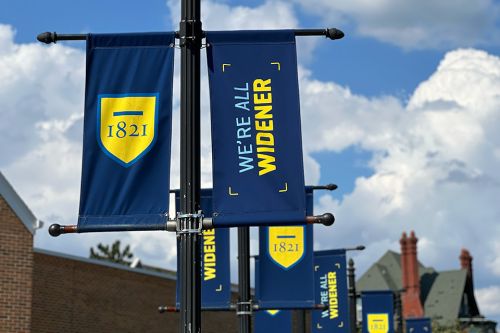 Blue and yellow We're All Widener streetlight banners on campus
