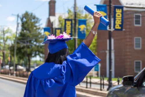 A female graduate in a cap and gown raises her diploma in the air.