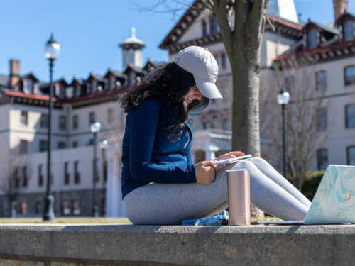 A female student uses a laptop outside the Old Main building on Widener University's campus.
