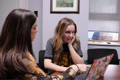 Julie Abrams and Inva Furriku work together on a laptop that is covered in stickers