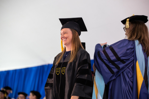 tara valoczki 960x640 Tara Valoczki stands on stage in black Commencement robe and hat