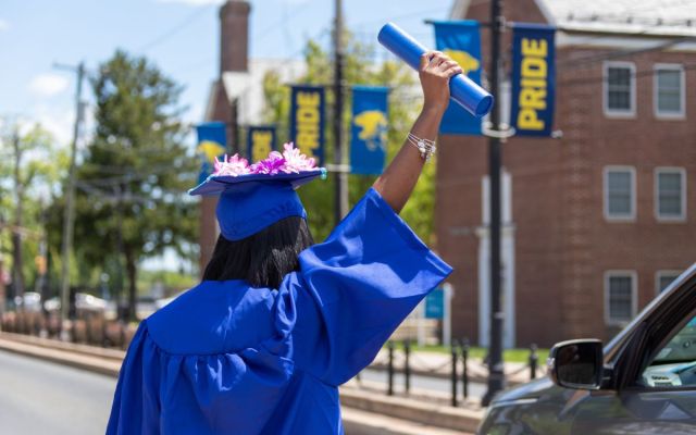 A female graduate holds her diploma tube up the air after crossing stage.