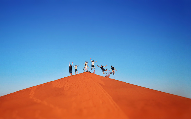 Group of students jumping in the distance on top of a sand dune